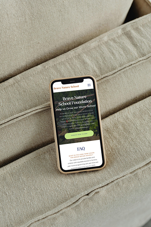 A smartphone rests on a textured beige sofa, displaying a school foundation website with a nature-themed image and FAQ section, conveying a calm, welcoming tone.