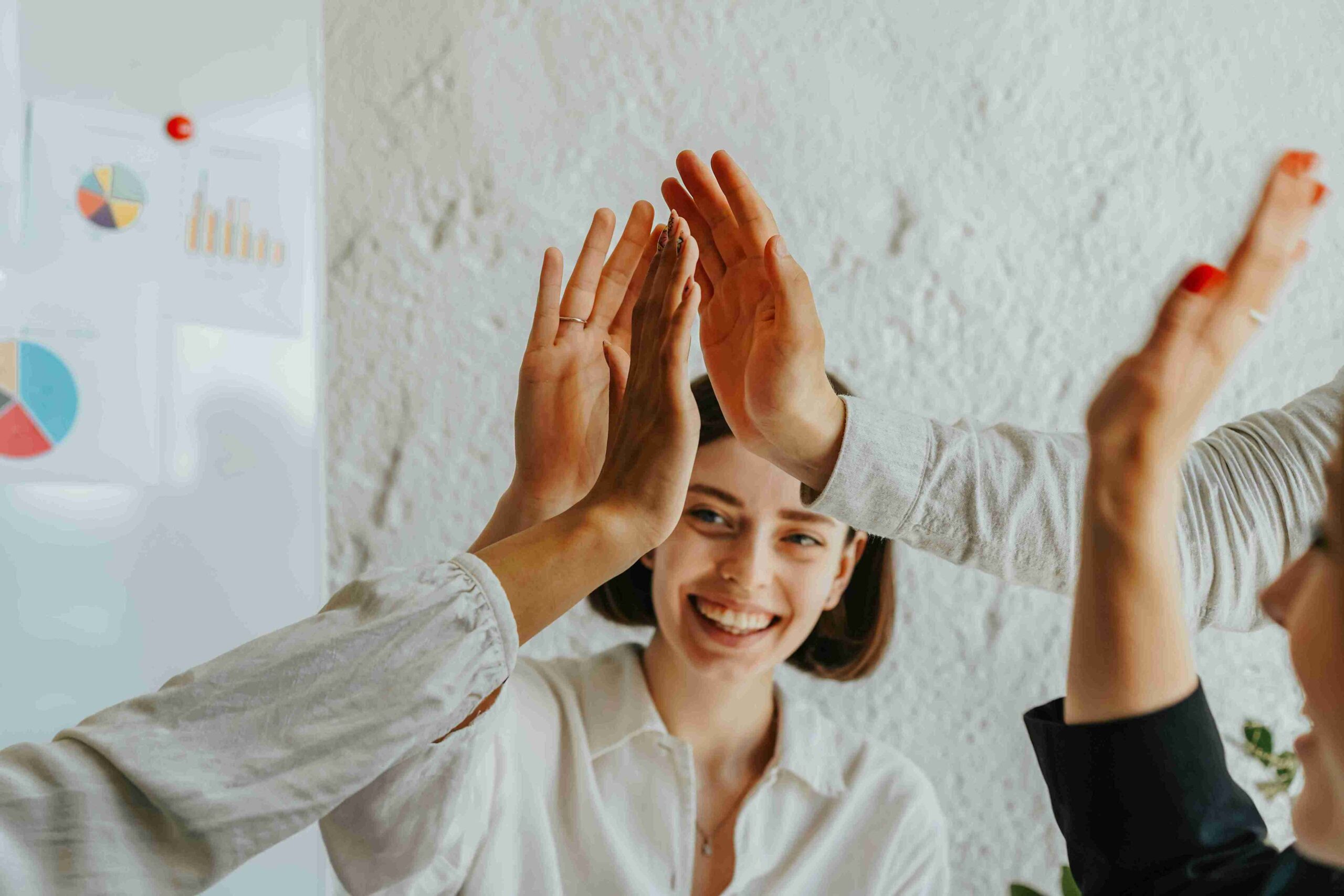 A group of business professionals celebrating success with high fives in a collaborative office environment.