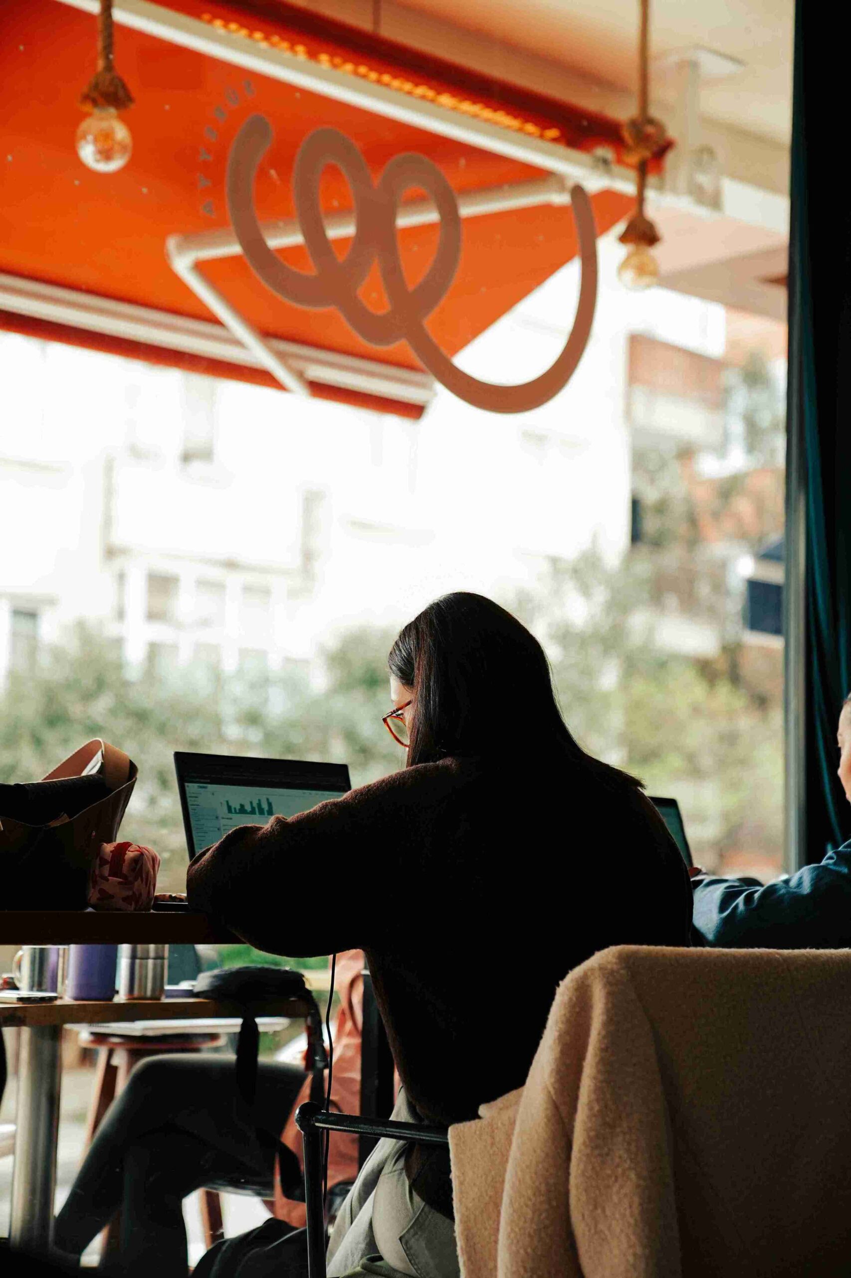 Woman working on SEO for a therapist website on her laptop in a coffee shop.