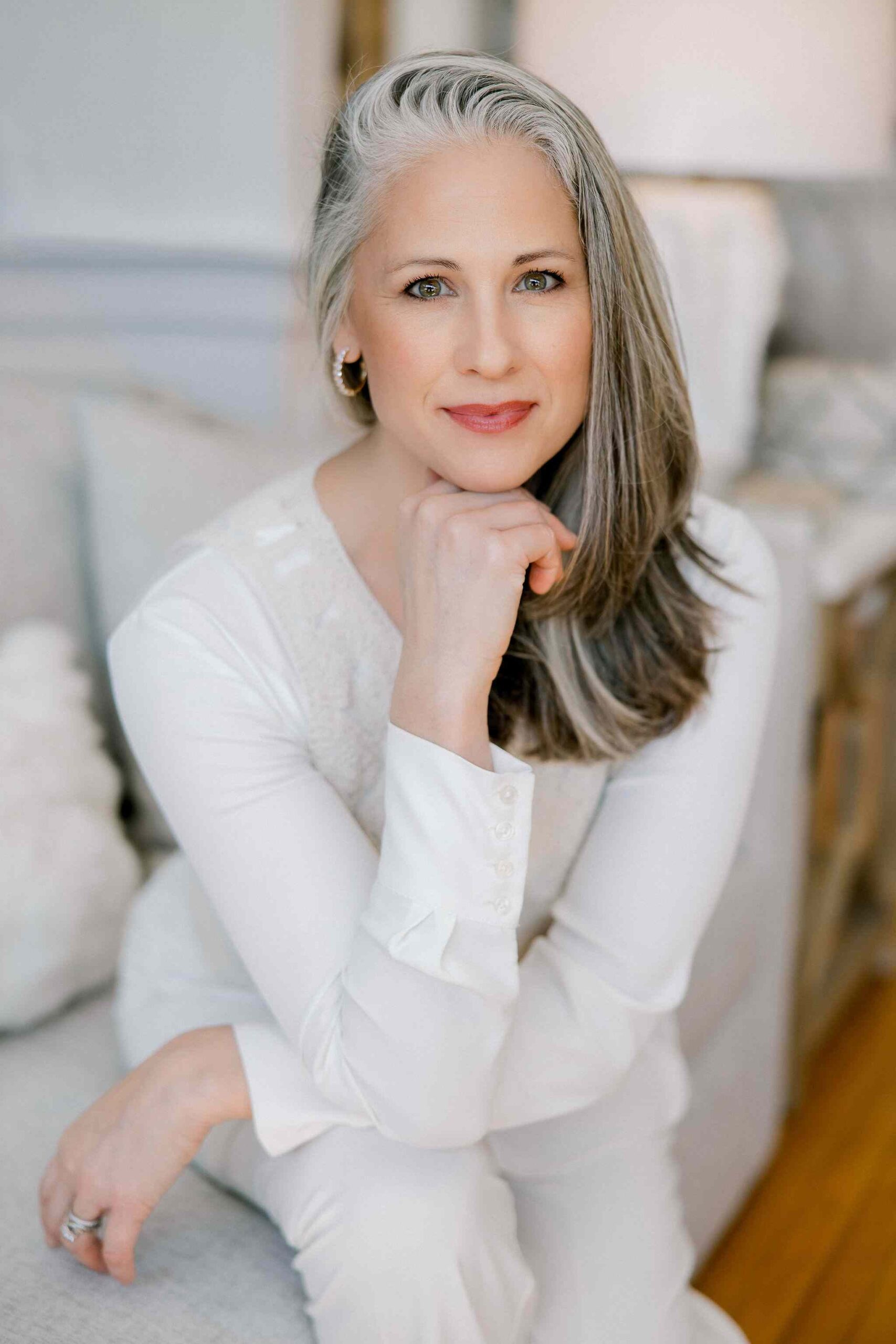 Woman during her brand shoot sitting on a coach with her elbow on her knee and head resting on her hand.