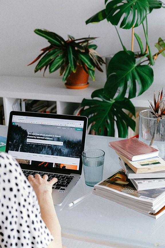 A woman sits at a desk, focused on her laptop, writing a blog post about how to Optimize images for Showit with a cozy workspace around her.