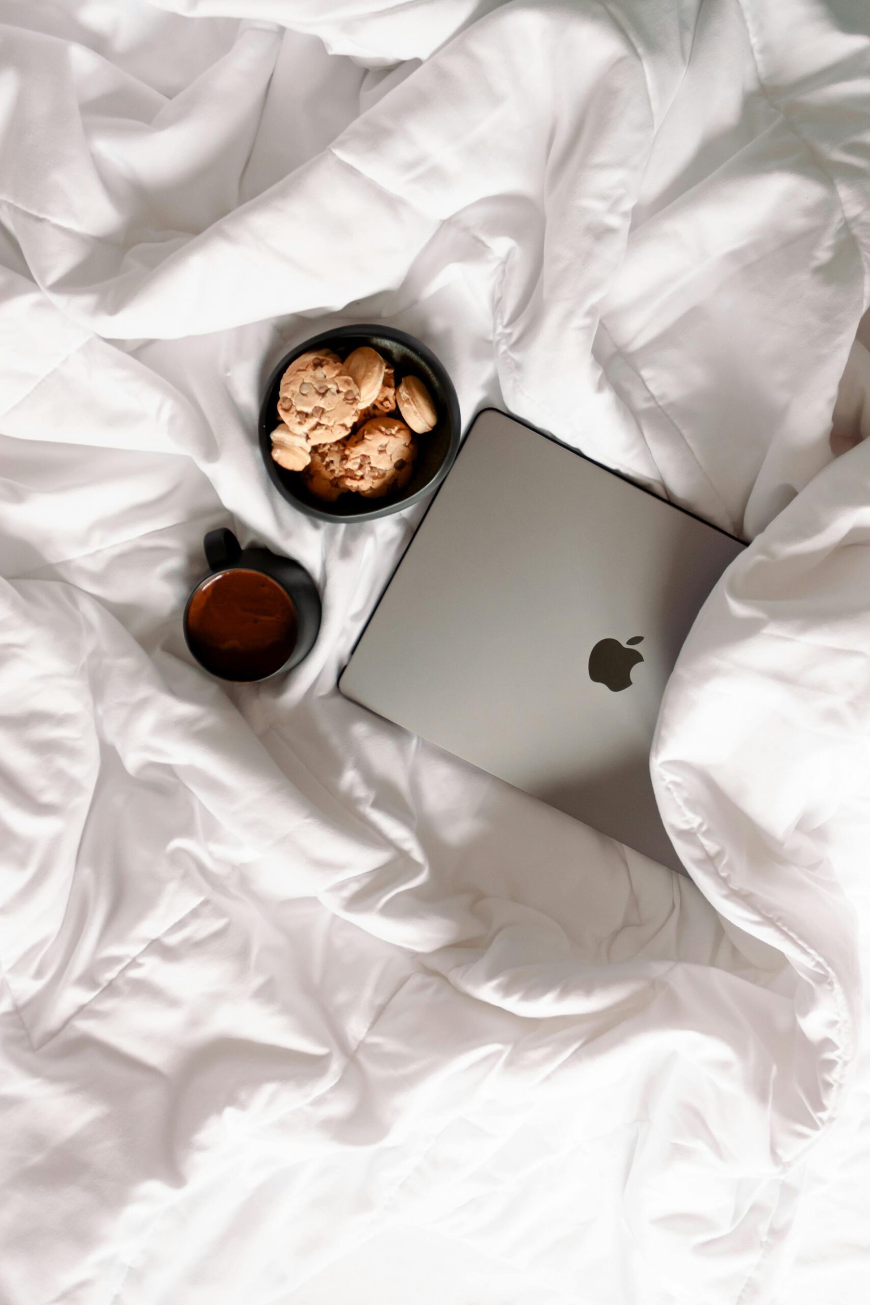 A laptop and a cup of coffee resting on a neatly made bed, creating a cozy workspace atmosphere.