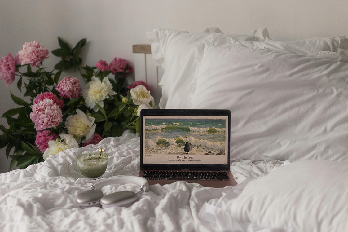 A laptop resting on a bed surrounded by colorful flowers and soft pillows, creating a cozy workspace vibe.