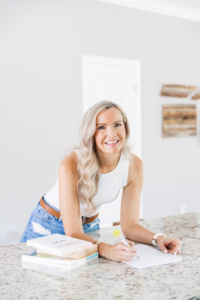 A copywriter named Alyssa B sits at a kitchen counter, writing notes with a pen and paper, focused on her work.