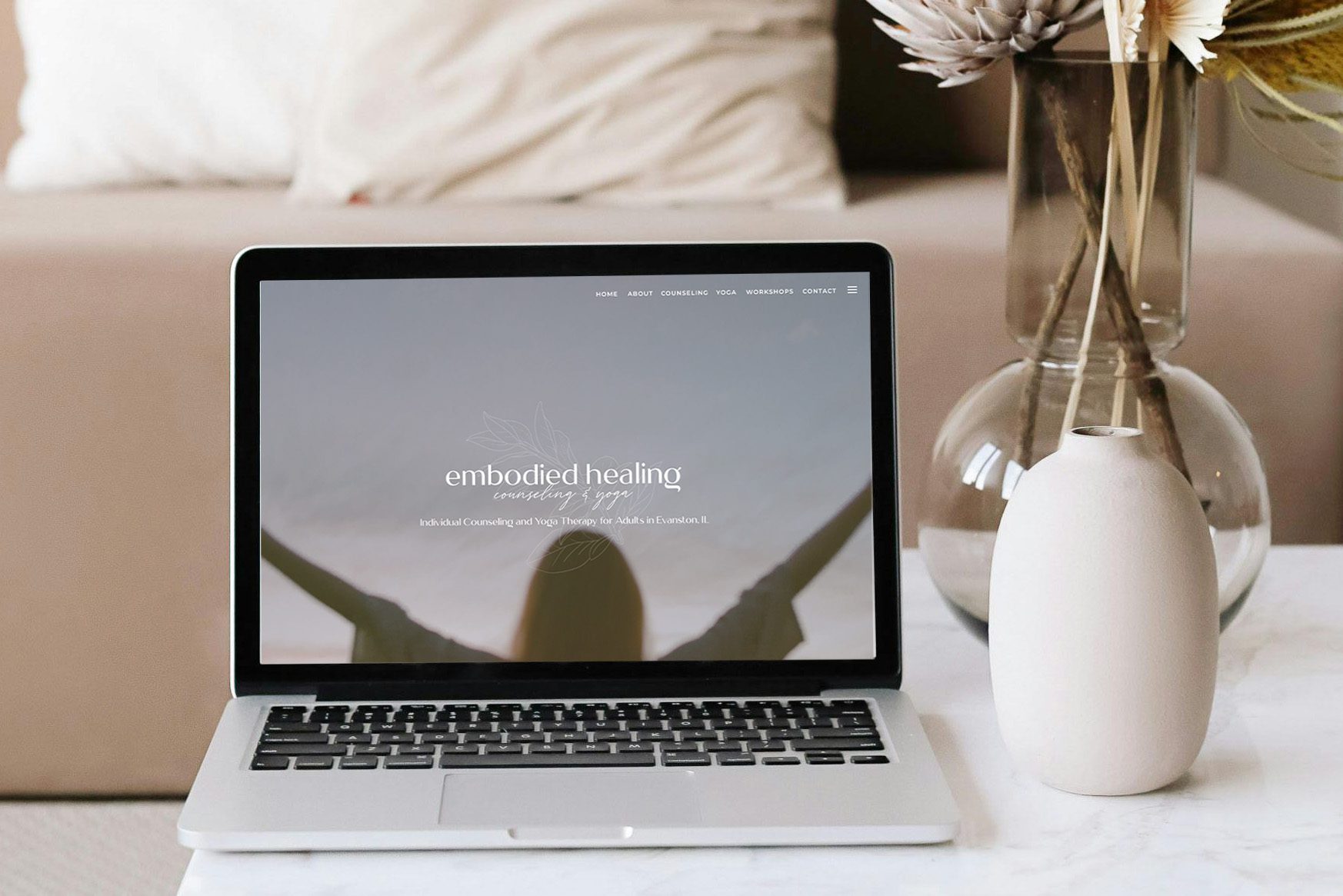 A laptop sits on a table next to a vase with a single flower, creating a cozy workspace atmosphere.