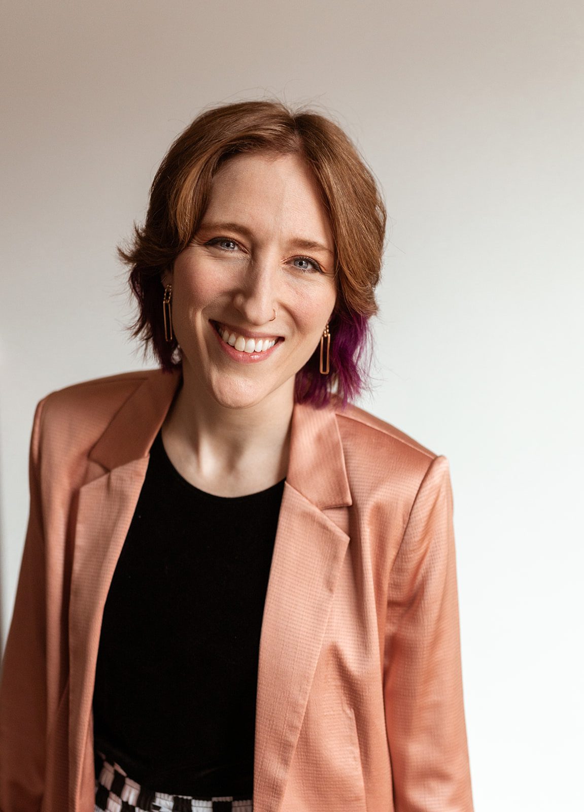 A woman named Taylor Cameron with purple hair wearing a stylish pink blazer.