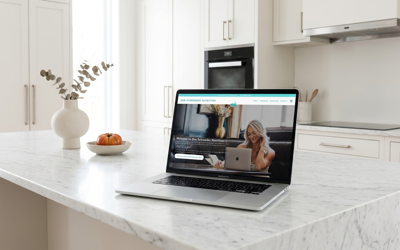Open laptop showing a lifestyle website with a smiling woman at a computer, resting on a marble kitchen island in a bright, elegant space.