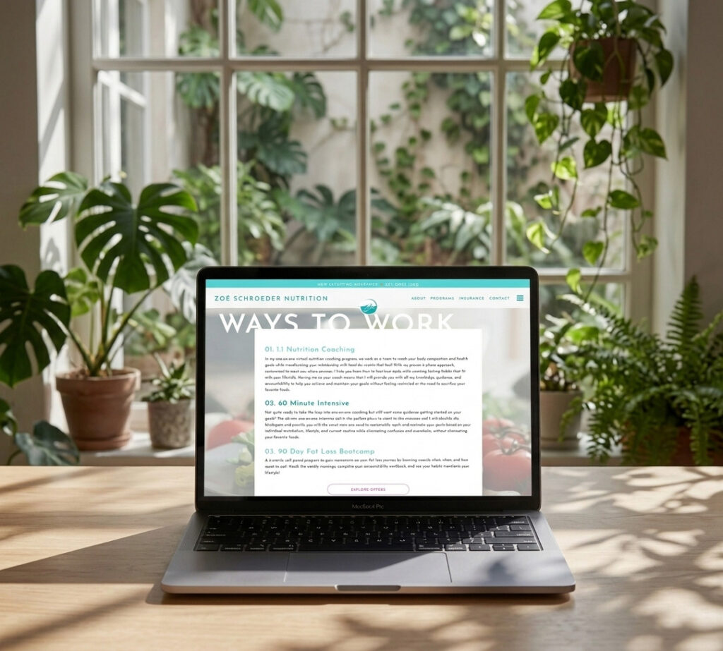 A laptop on a wooden table displays a nutrition website against a backdrop of large, bright windows with lush green plants. The scene feels fresh and inviting.