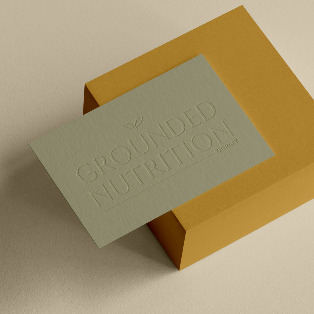 Embossed “Grounded Nutrition” card rests on a mustard-yellow envelope, creating a minimalist, warm, earthy wellness impression.