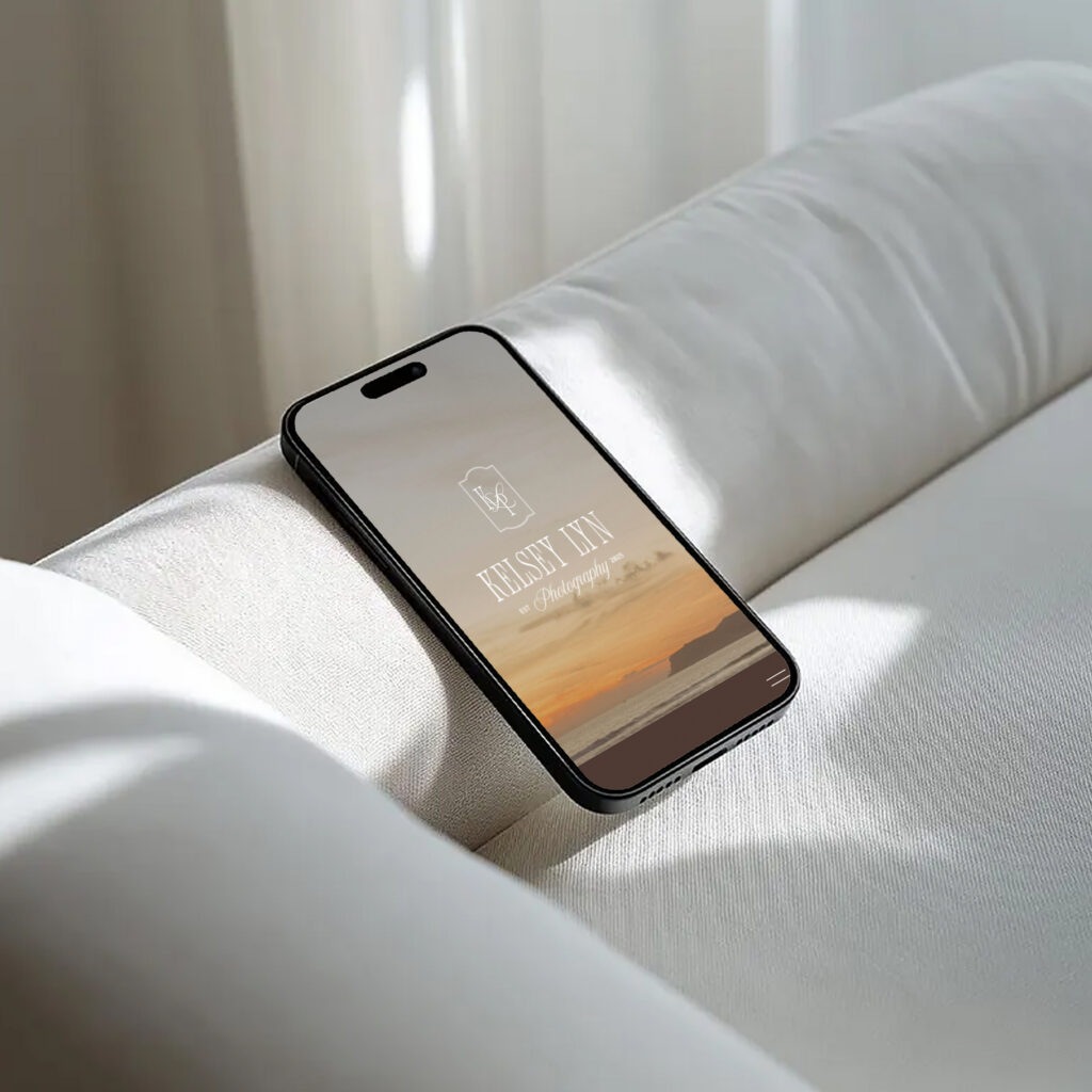 A black smartphone rests diagonally on a white bed, its screen showing a minimalist sunset lock screen; the muted scene feels calm and serene.