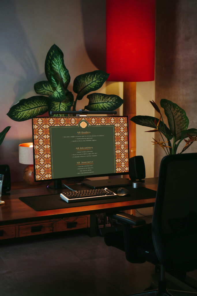 Cozy home office with leafy plants, a patterned monitor displaying text, keyboard, and glowing red lamp in warm, moody light.