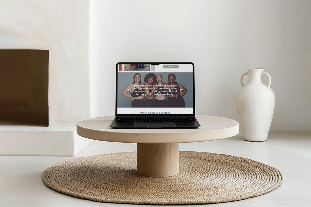 Minimalist living room with a laptop showing a webpage on a round wood table, beside a white vase and woven rug; calm, modern mood.