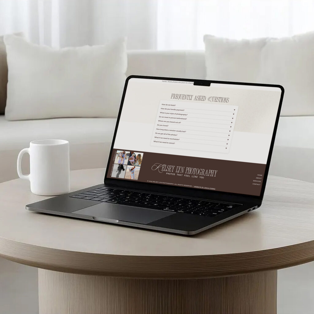 A laptop displaying a minimalist photography portfolio sits on a round wooden table beside a white mug, in a bright, calm workspace.