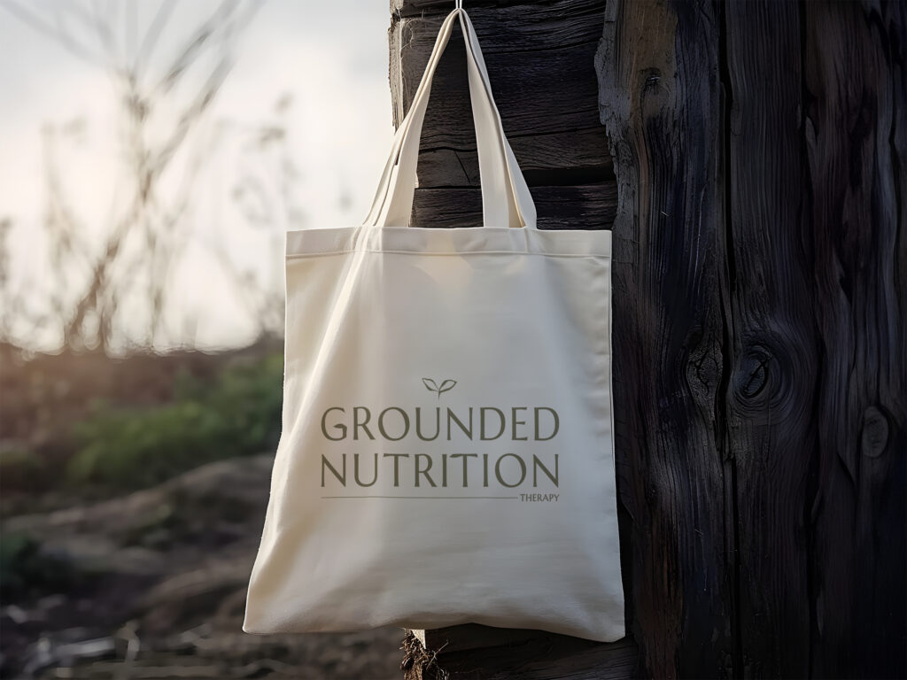 Cream canvas tote labeled “Grounded Nutrition” hangs on a rustic wooden post outdoors, evoking a calm, natural wellness mood.