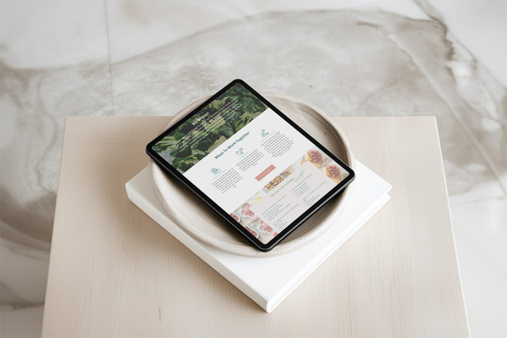 iPad showing a colorful webpage rests on stacked white books atop a light wood table, creating a calm, minimalist scene.