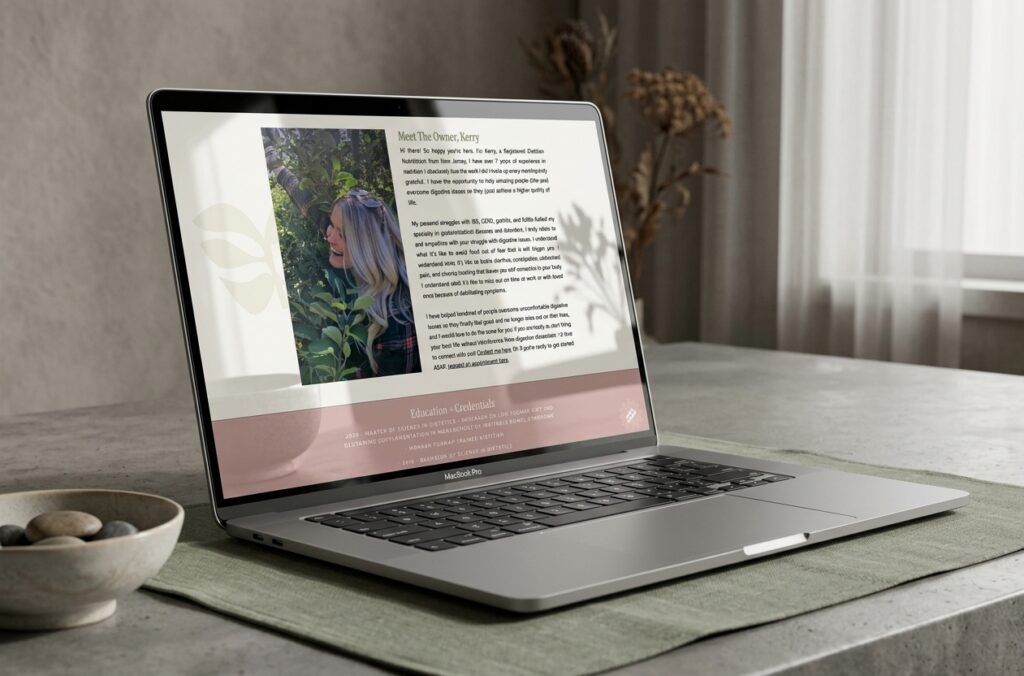 Open laptop on a marble table displays a fashion video, with a cream sofa, curtains, bowl, and dried flowers creating a cozy setting.