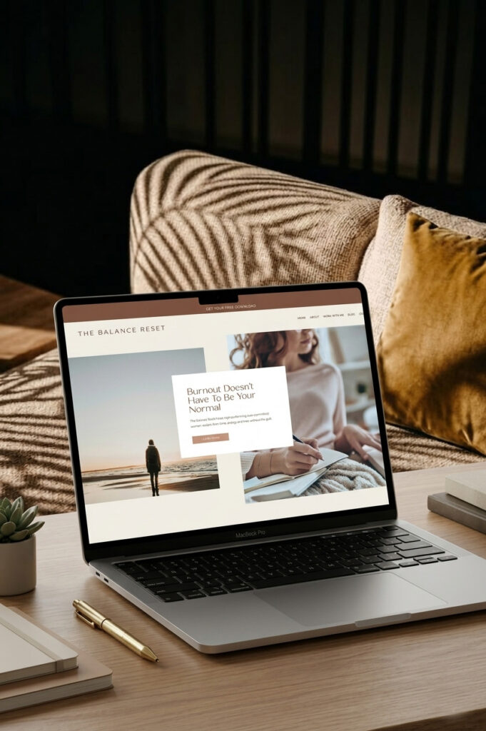 A laptop on a wooden table displays a wellness website with beach imagery and a woman journaling; warm pillows and soft light create a calm, restorative mood.