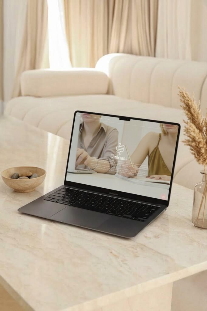 Open laptop on a marble table displays a fashion video, with a cream sofa, curtains, bowl, and dried flowers creating a cozy setting.