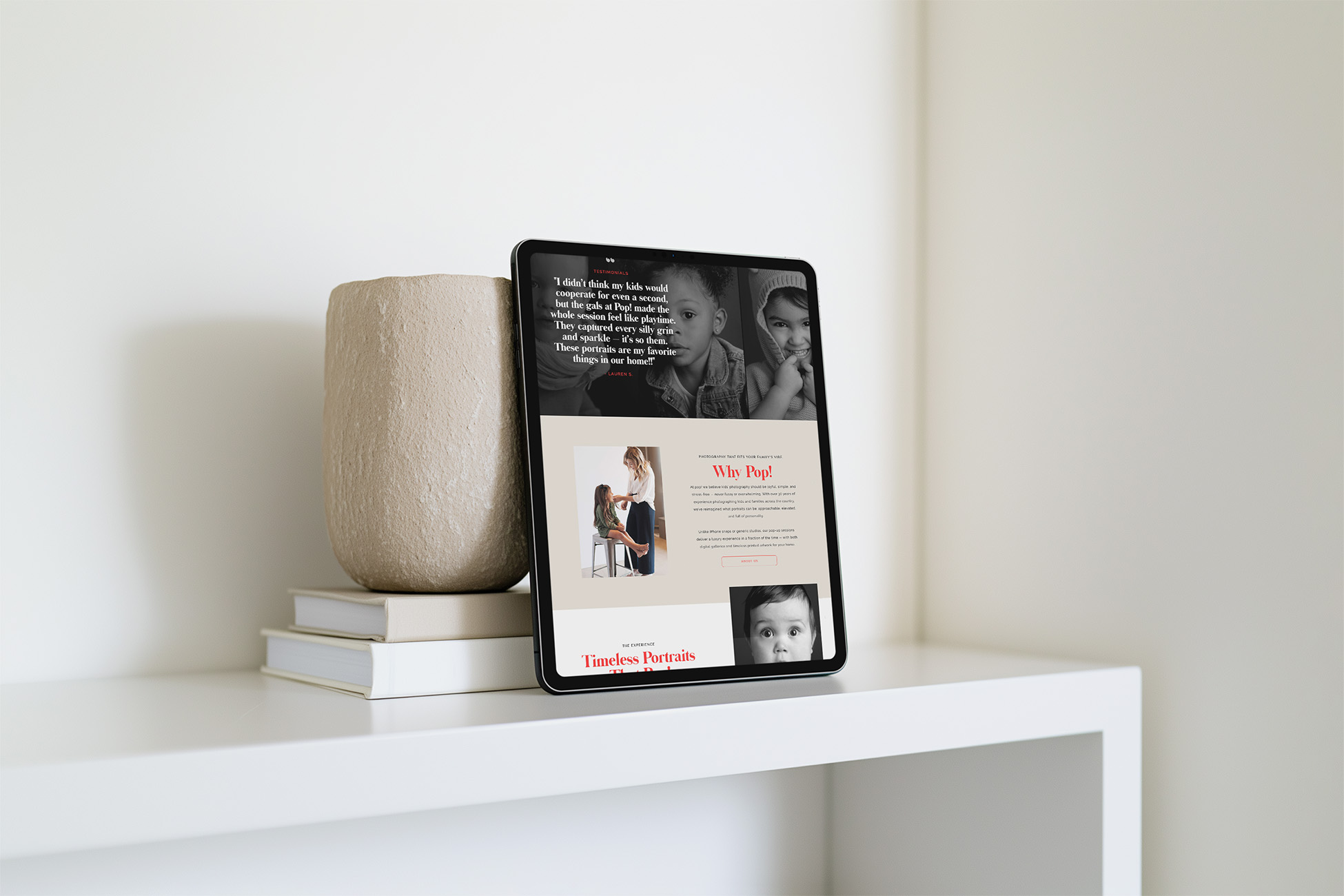 Tablet displaying a family-focused webpage with children’s photos rests against a beige vase and books on a white shelf, creating a calm, modern scene.