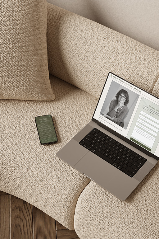 Overhead view of a laptop displaying a grayscale portrait and webpage beside a smartphone on a textured beige sofa, creating a calm work setting.