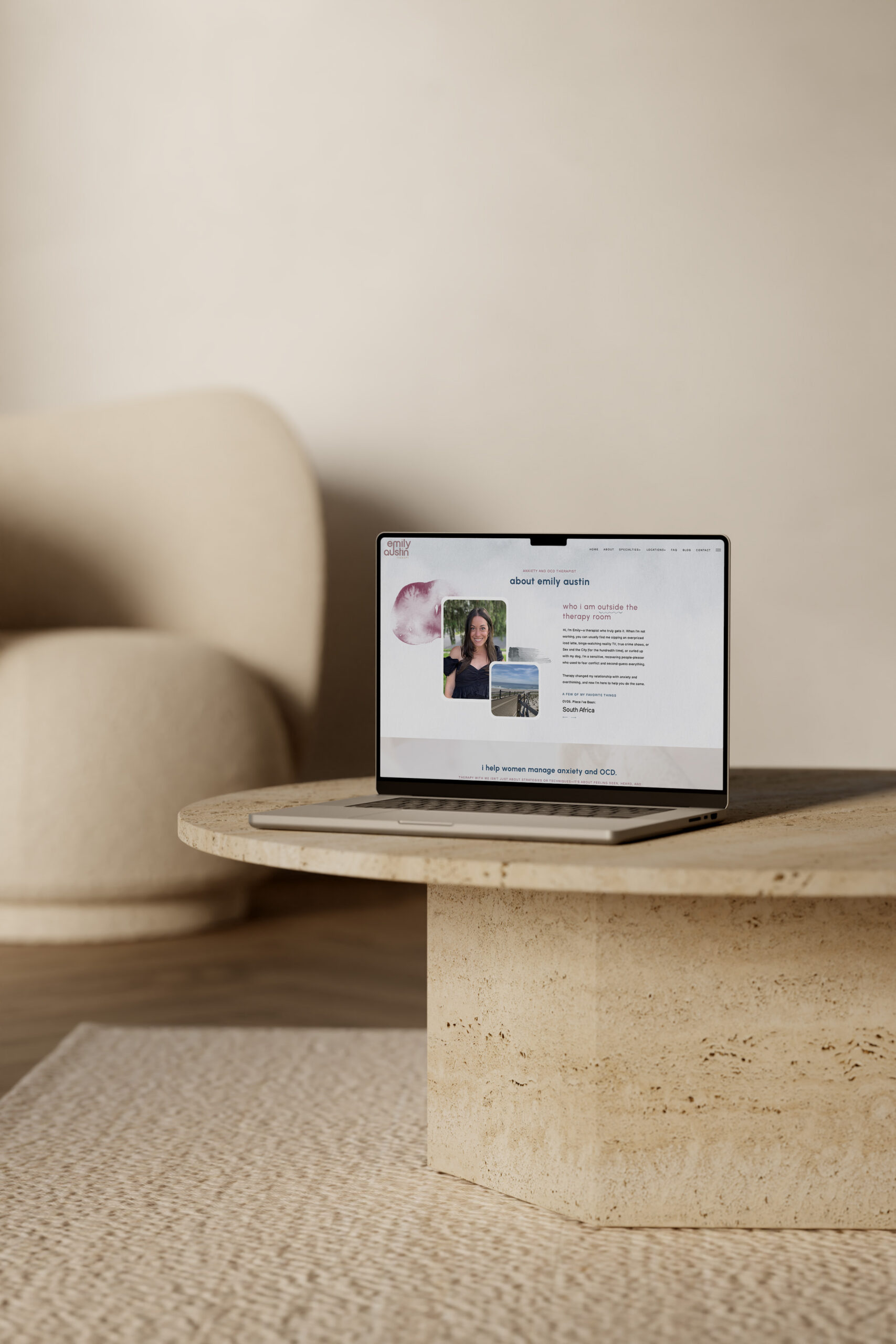 Laptop displaying a webpage with portraits sits on a stone coffee table in a neutral living room, beside a cream sofa; warm, calm atmosphere.
