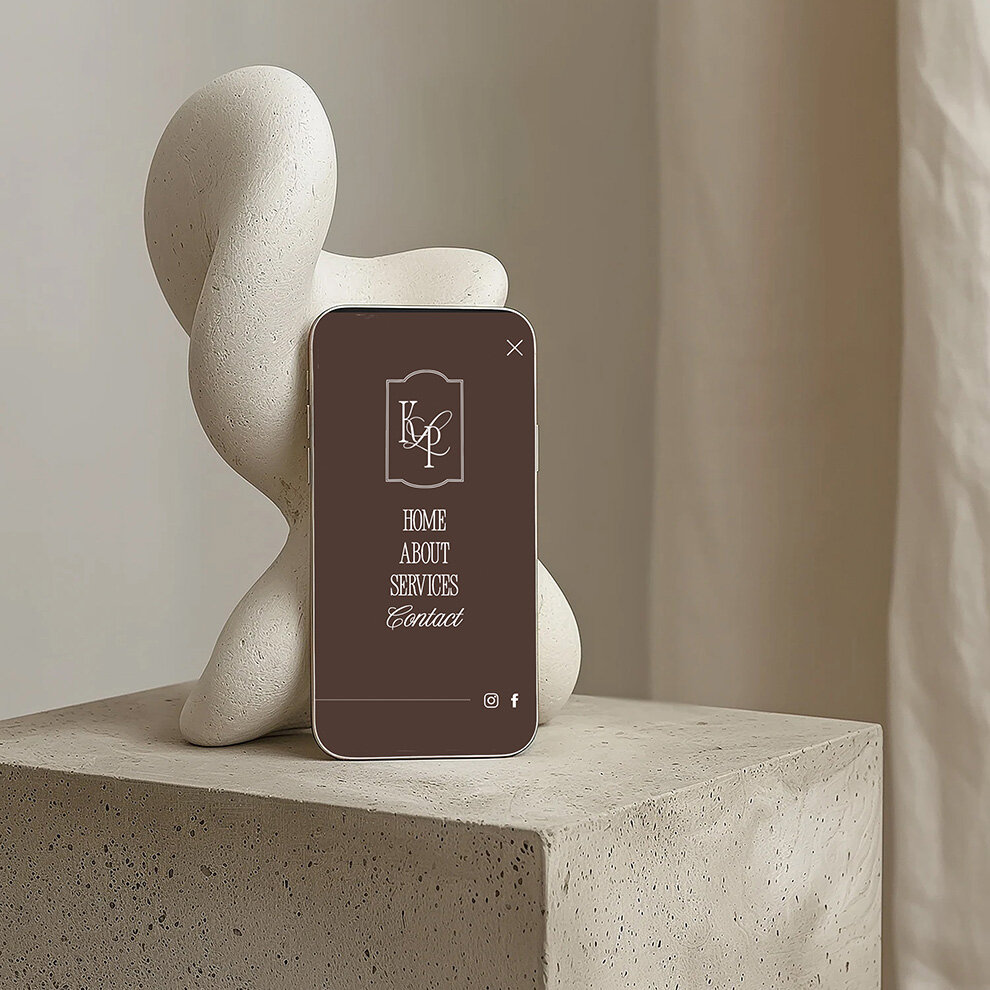 Minimalist scene with a brown “Home About Services Contact” phone screen beside an abstract white sculpture on a concrete pedestal.