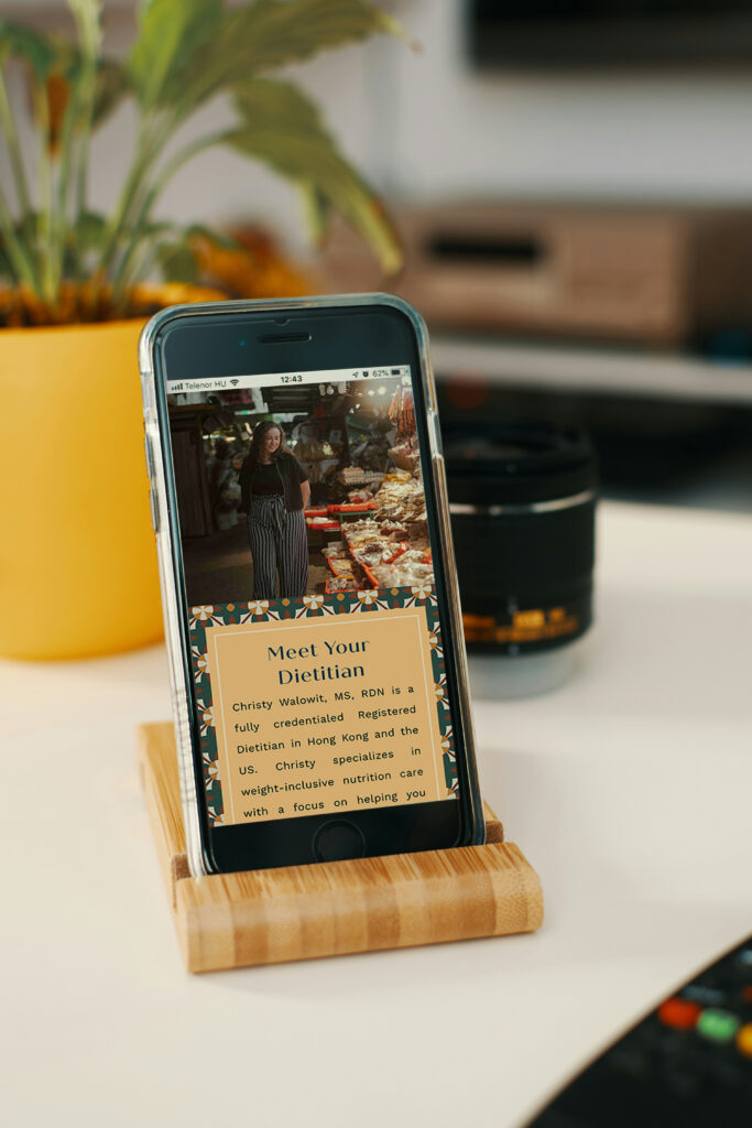 Smartphone on a wooden stand displays a dietitian article beside a yellow potted plant and camera lens, creating a warm, informative scene.