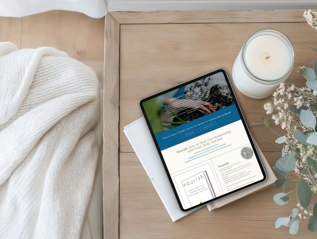 Overhead view of a tablet displaying a wellness website on a wooden table, beside a white candle, eucalyptus sprigs, and a cozy knit blanket.