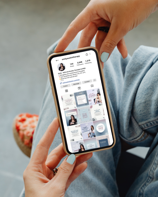 Hands with turquoise nails hold a smartphone displaying an Instagram profile and post grid, against a relaxed background of jeans and sneakers.