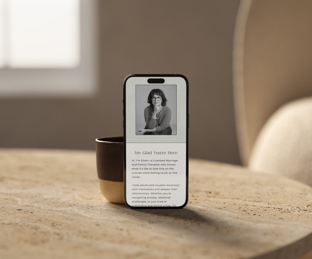 Smartphone displaying a grayscale woman’s portrait and welcome text stands in a coffee mug on a wooden table, creating a warm, inviting mood.