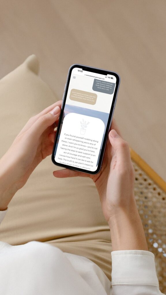 Woman sitting cross-legged, using an iPhone to send a message, promoting mindfulness and communication in therapy.