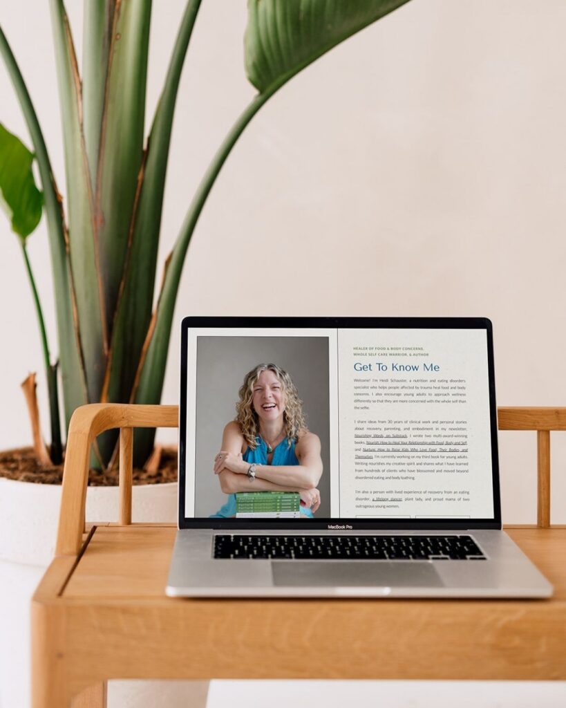 Laptop displaying a cheerful woman and “Get to Know Me” article, set on a wooden desk beside a tall green houseplant in a bright room.