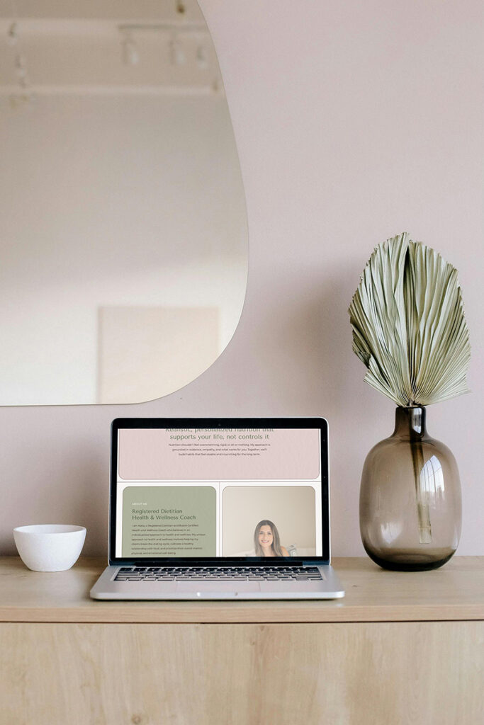 Minimalist home office with a laptop displaying an online lesson, beside a glass vase with dried leaves, in soft neutral tones.