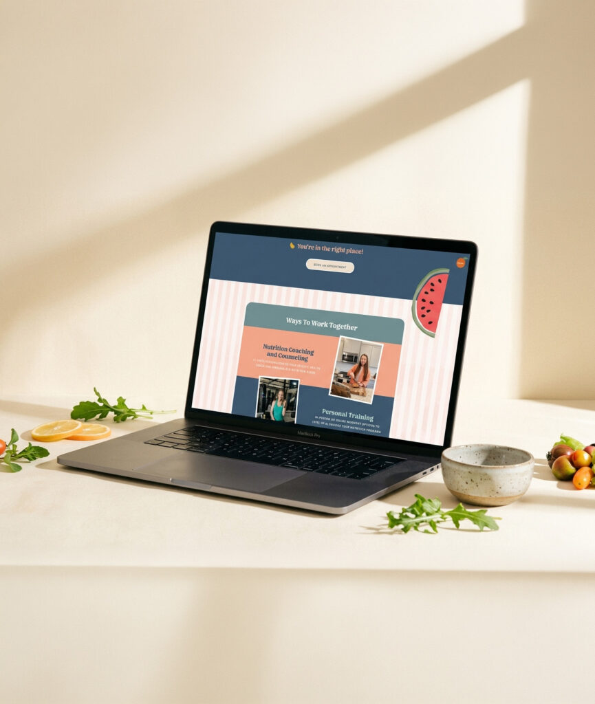 Laptop displaying a colorful travel webpage on a sunlit table, with coffee, fruit, and greens nearby; warm, calm workspace atmosphere.