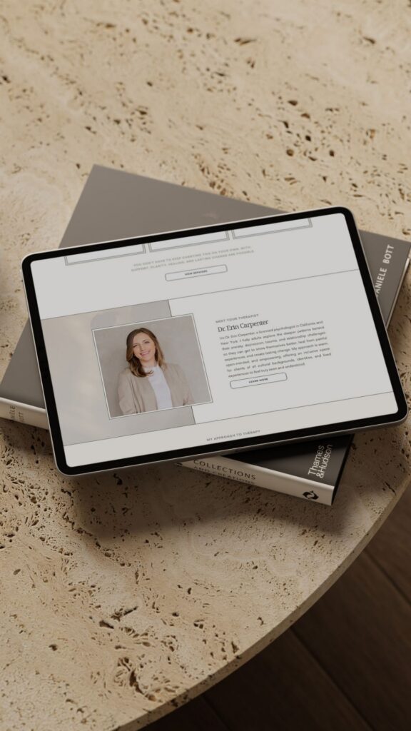 Tablet displaying a professional profile webpage with a woman’s portrait, resting on stacked books atop a textured stone table in warm light.