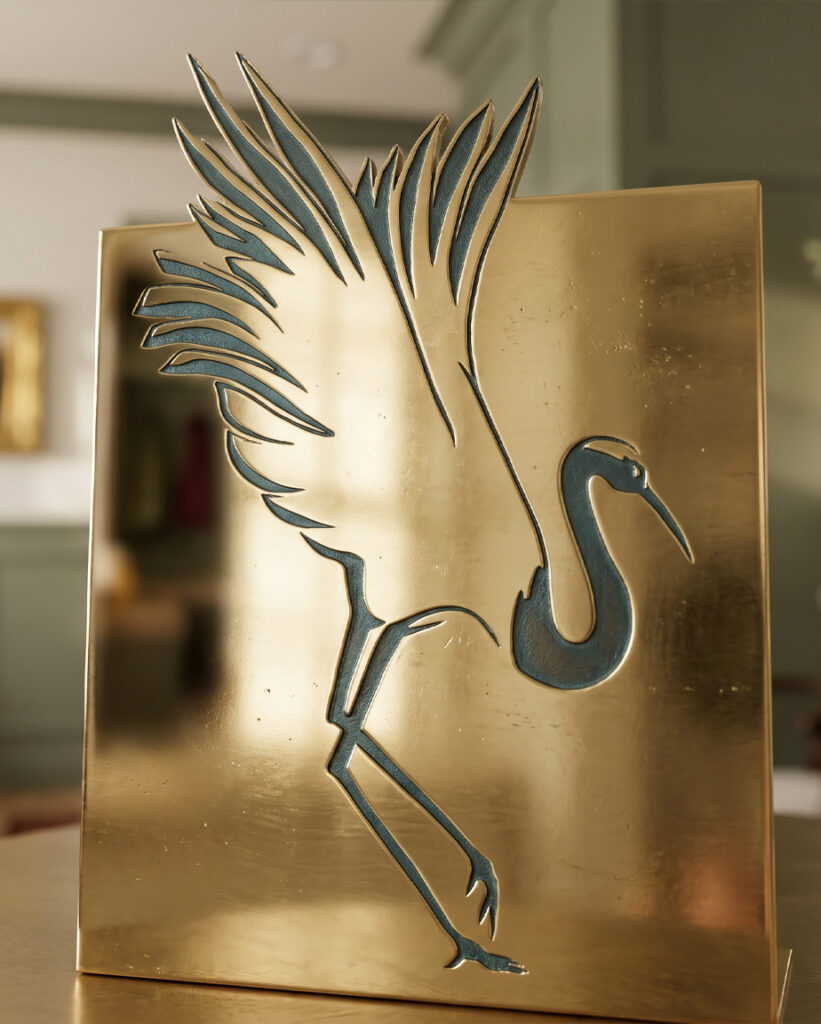Gold-toned metal artwork featuring a stylized heron with sweeping feathers and a long curved neck, creating an elegant, serene atmosphere.