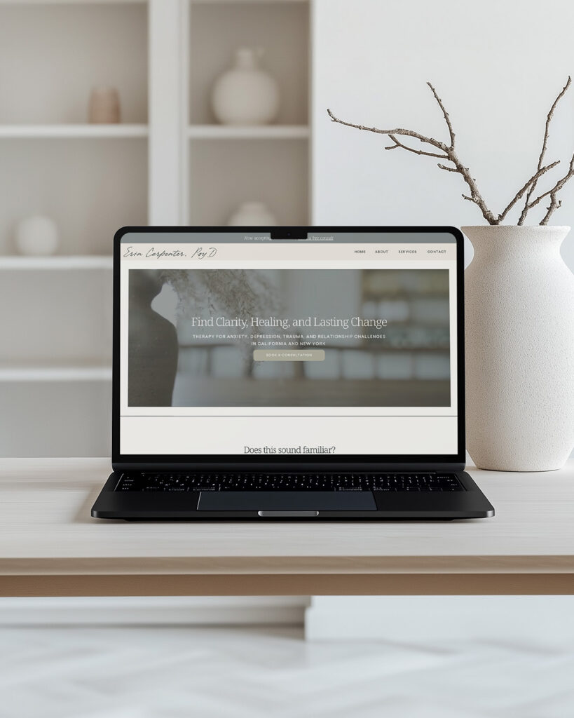 Laptop displaying a calm wellness website on a light wood desk, beside a white vase with branches in a minimalist room; serene, inviting mood.