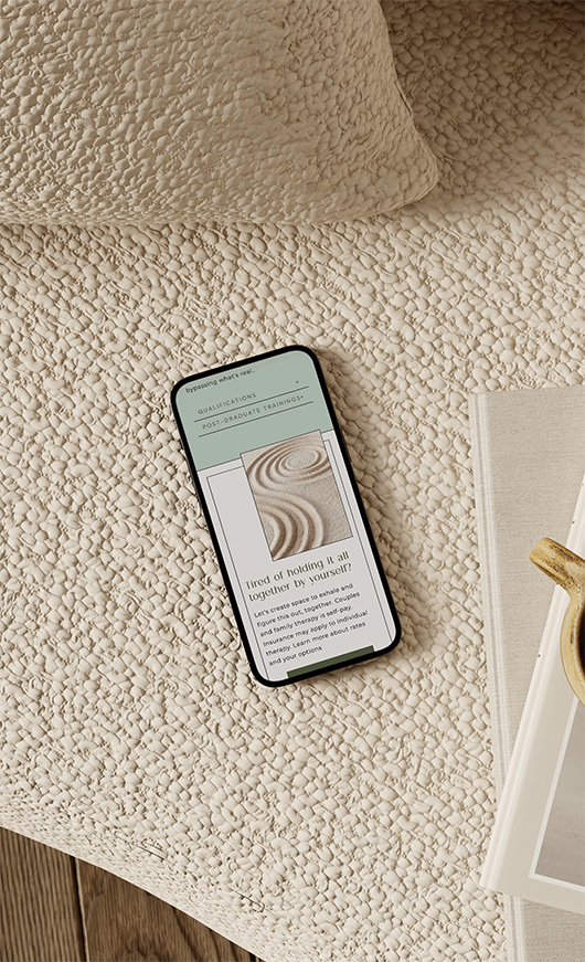 Smartphone displaying a design article and abstract spiral image rests on a cream textured rug beside a neutral book, creating a cozy scene.
