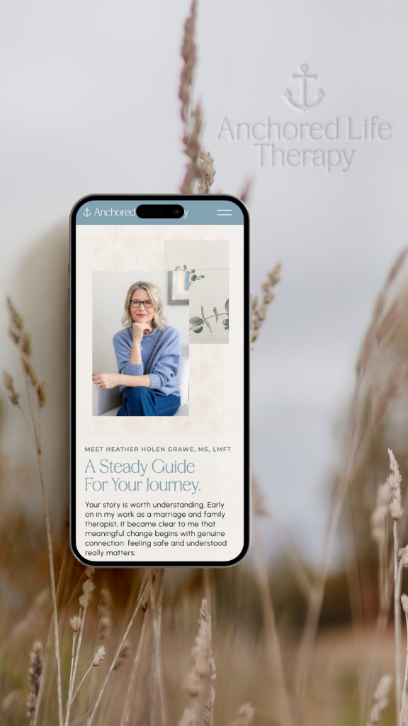 Smartphone showing Anchored Life Therapy website with a smiling woman and wellness article, set against soft, calming dried grasses.