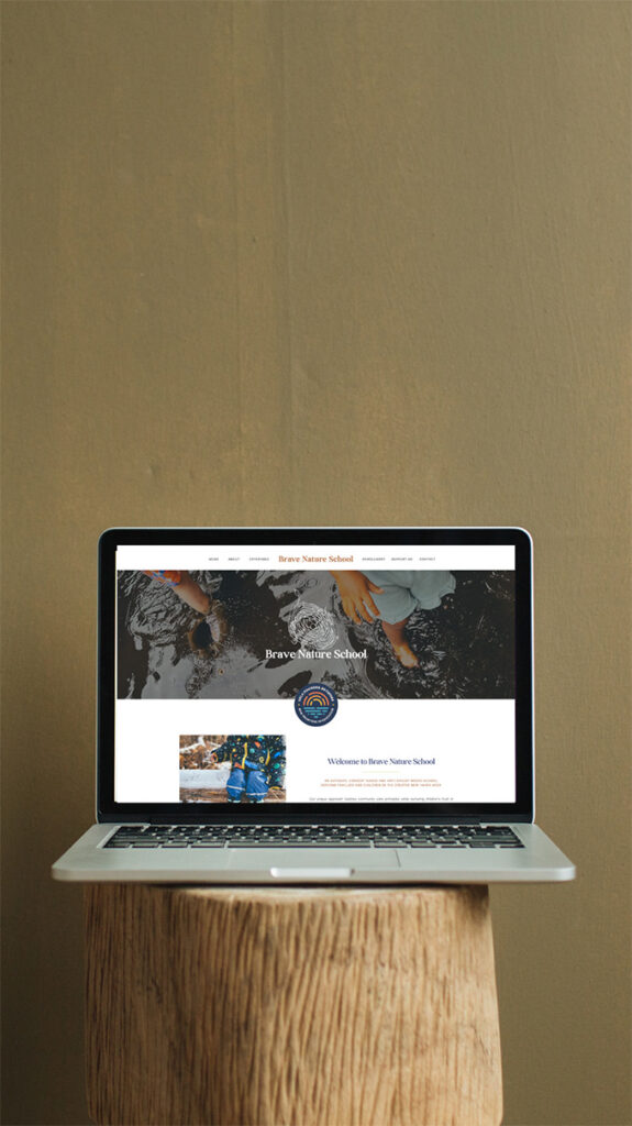 A laptop on a wooden stump displays a school website, with a scenic banner and student photos; the minimalist setting feels calm and understated.