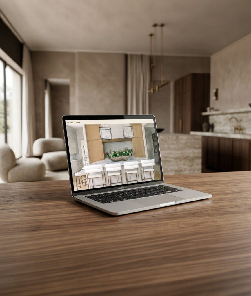 An open laptop displays a bright kitchen design with island seating, set on a wood table in a serene, modern neutral-toned home.