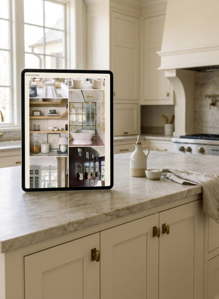 A tablet on a marble kitchen island displays a collage of refined interiors, including shelves, glass cabinets, and a blush-pink sink in a bright cream kitchen.