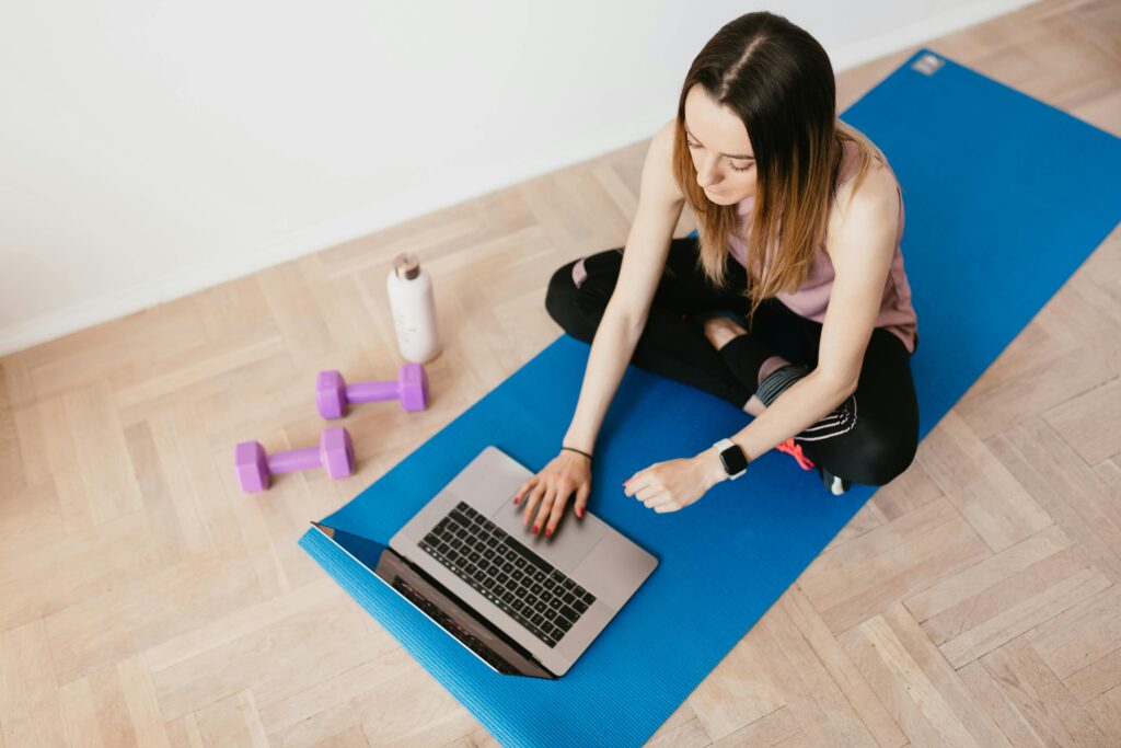 Woman on a yoga mat working on a MacBook Pro, combining wellness and productivity.